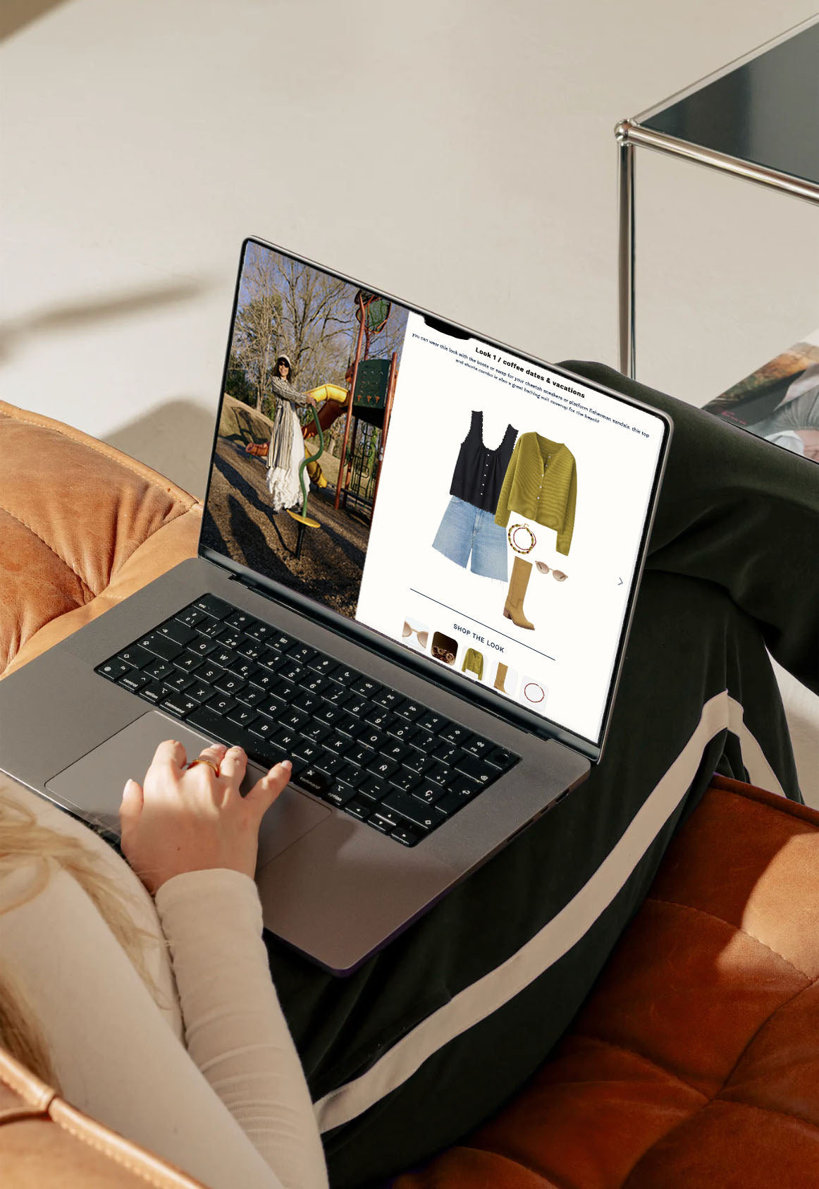 A person lounging on a bed with a laptop on their lap displaying a website featuring a summer capsule wardrobe with various clothing items and accessories.