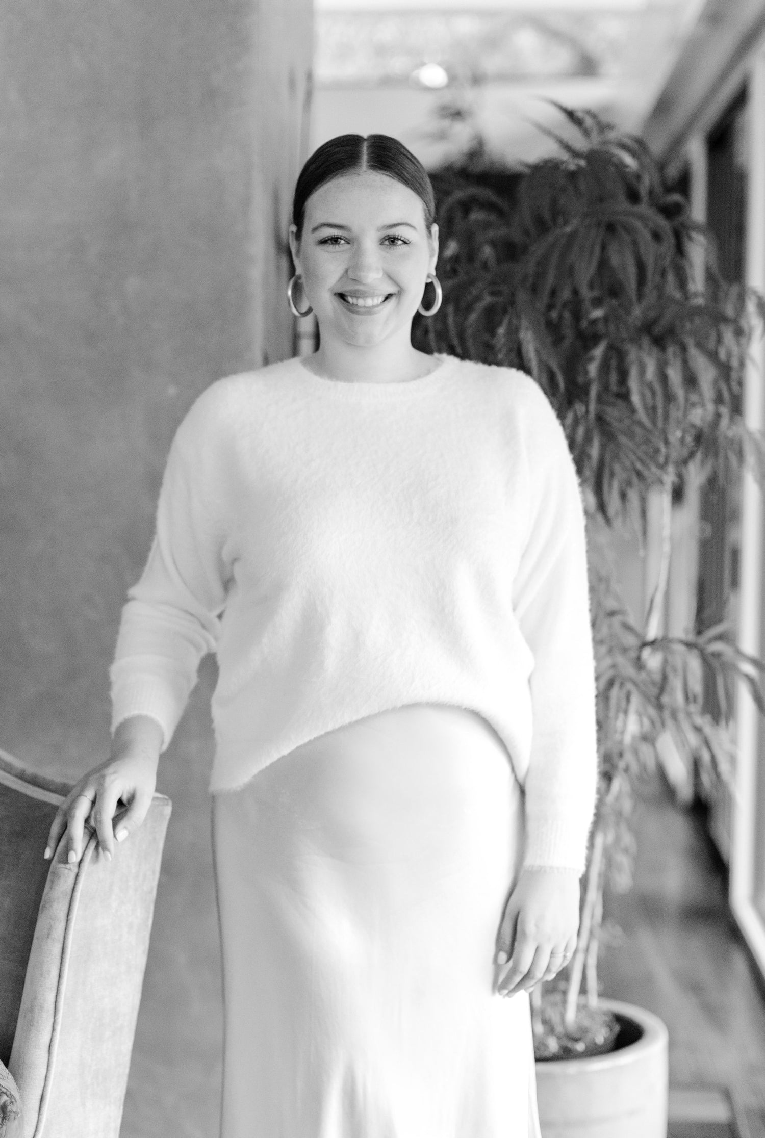 woman standing with her hand on a chair next to her wearing a sweater and skirt