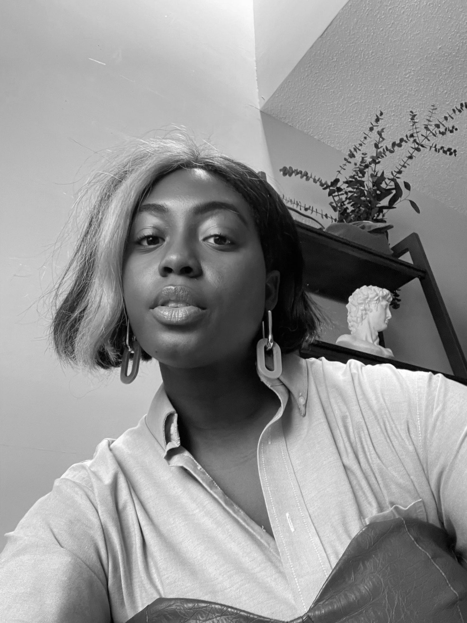 woman looking down into the cameral wearing dangly earrings and a button down shirt