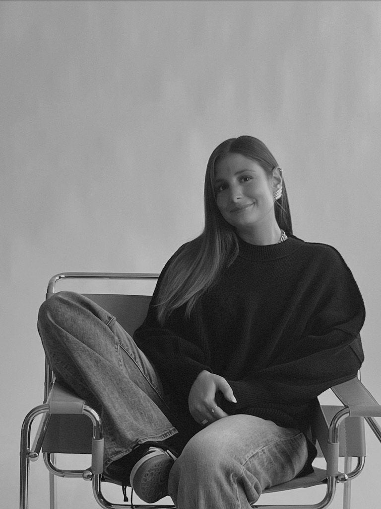 woman sitting in a chair with one leg up wearing a sweater, jeans, and sneakers