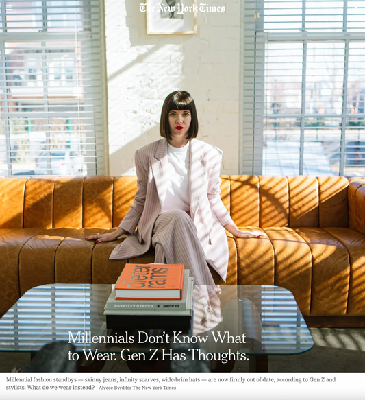 Woman sitting on a brown leather couch wearing a pinstripe suit in front of a coffee table with books stacked on top