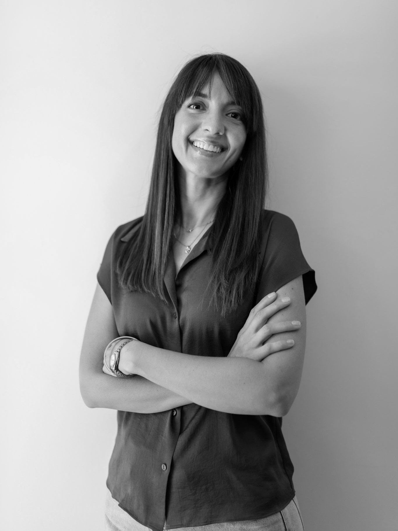 woman standing with her arms crossed, smiling wearing a short sleeve button down top