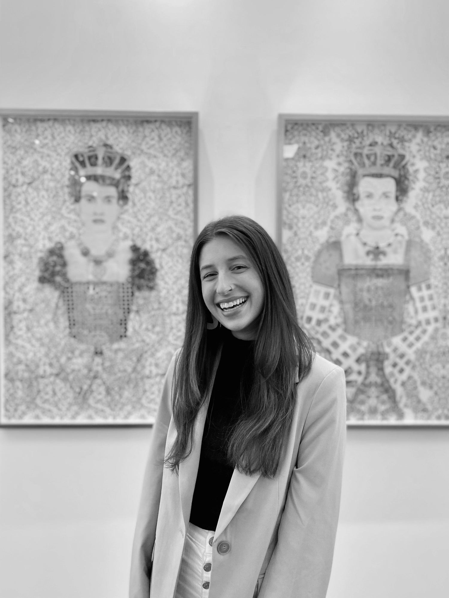 woman standing in front of two pieces of art, smiling wearing a shirt and blazer