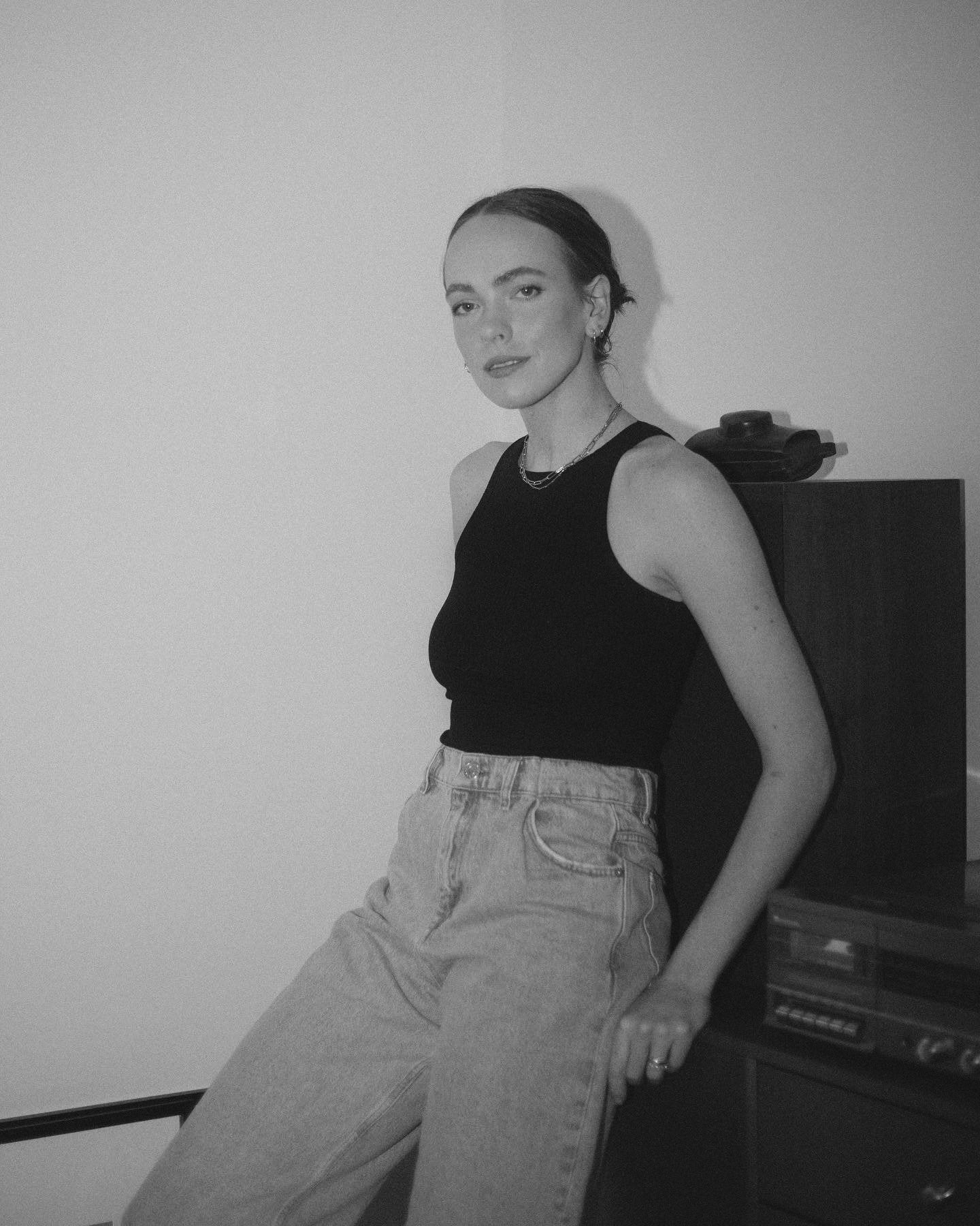 woman leaning back onto furniture wearing a tank top and jeans